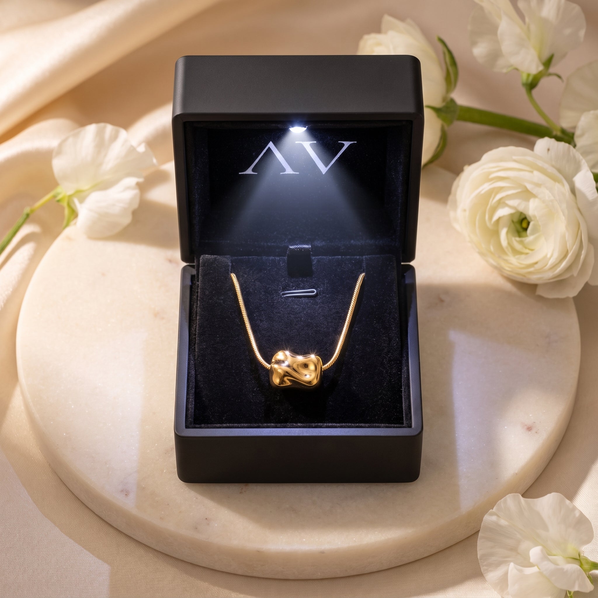 18K gold finish Petra necklace presented in a black LED-lit jewelry gift box on a marble surface.