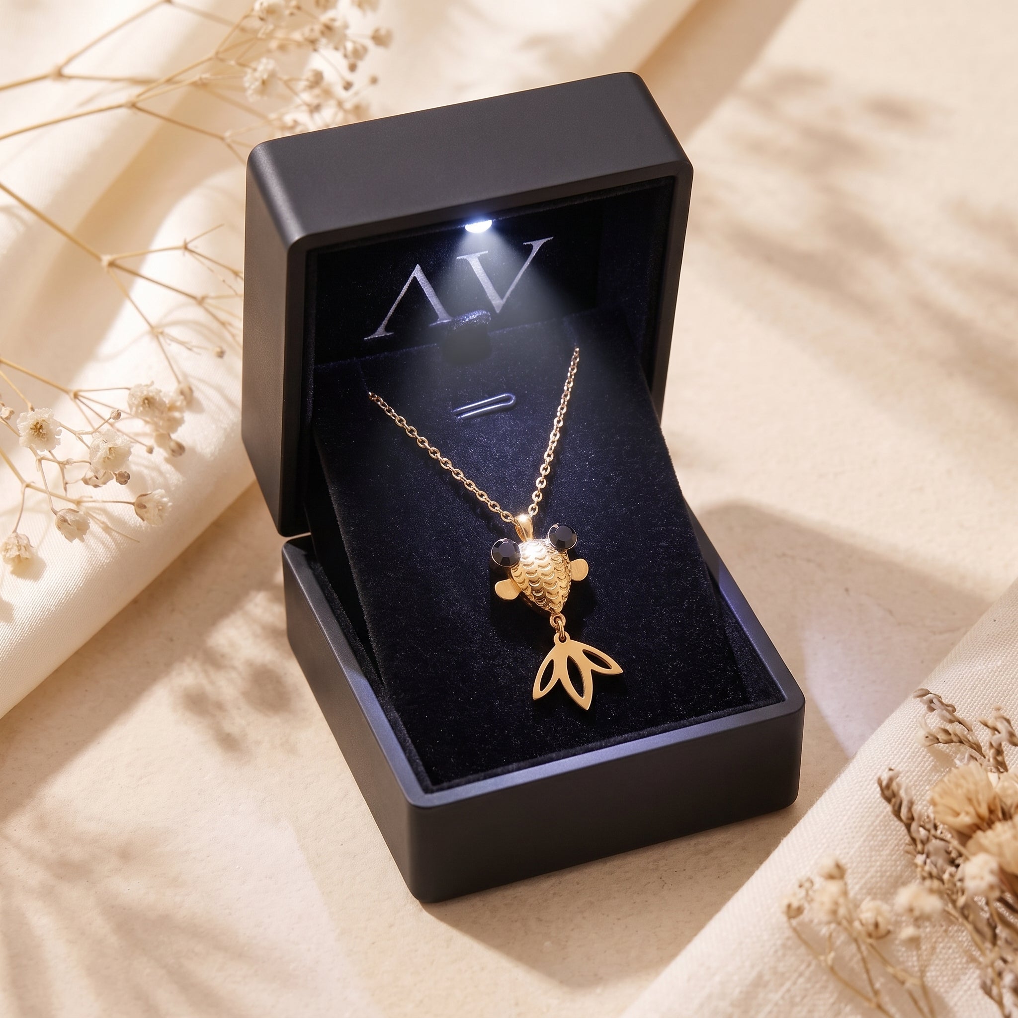 Gold finish goldfish necklace presented in a black lighted jewelry box on a neutral background.