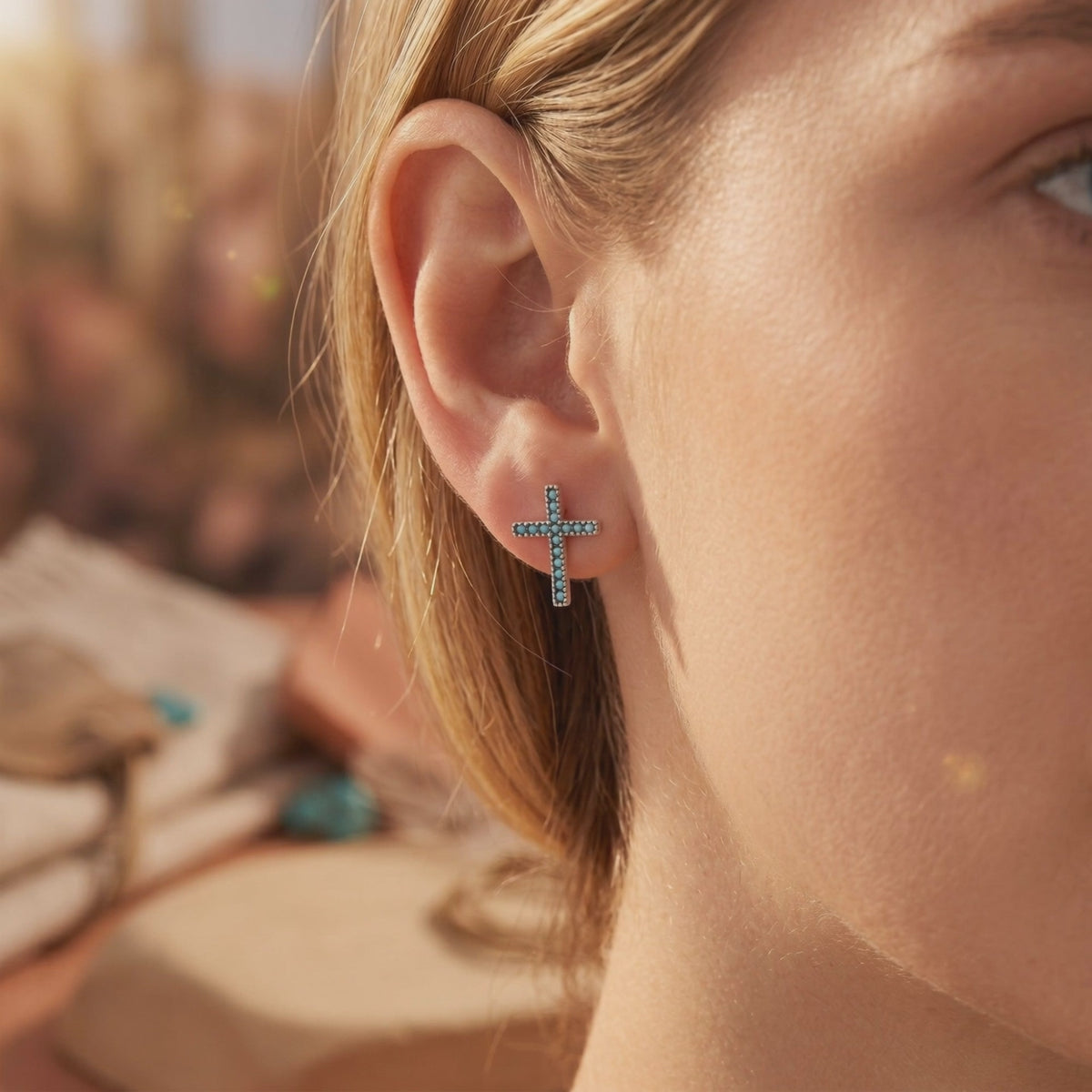 Close-up of one silver cross earring with blue stones worn on an earlobe