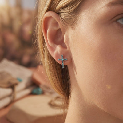 Close-up of one silver cross earring with blue stones worn on an earlobe