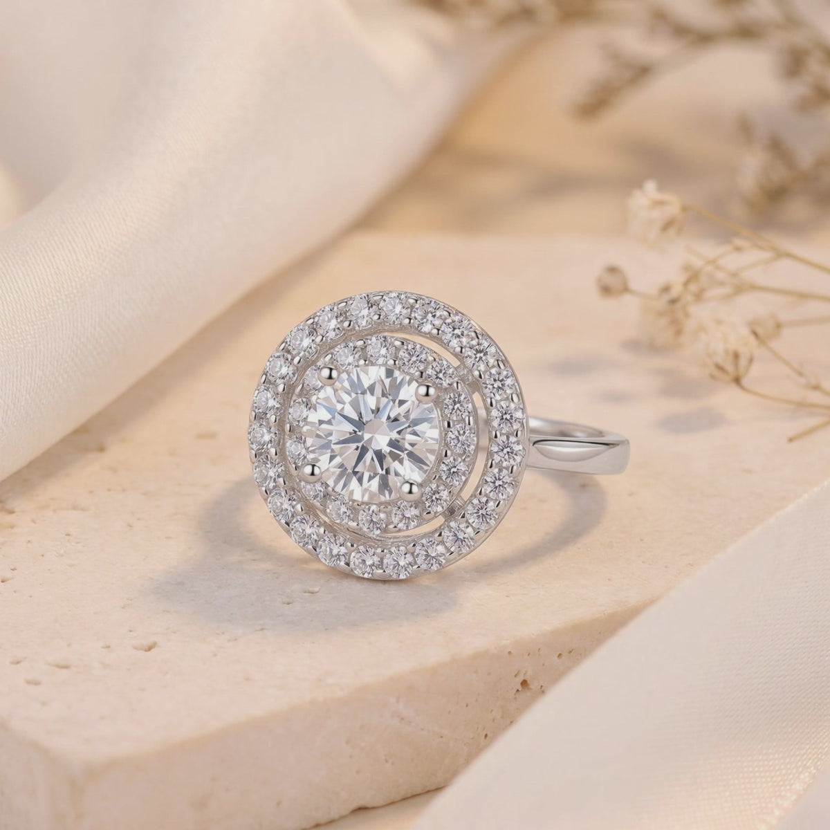 Close-up of the silver double halo solitaire ring with a round center stone resting on a stone surface.