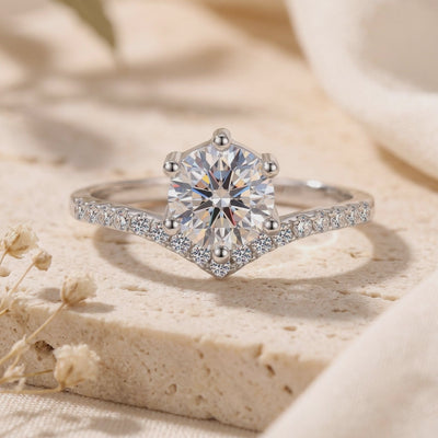 Close-up frontal view of a silver chevron solitaire ring resting on a textured stone surface.