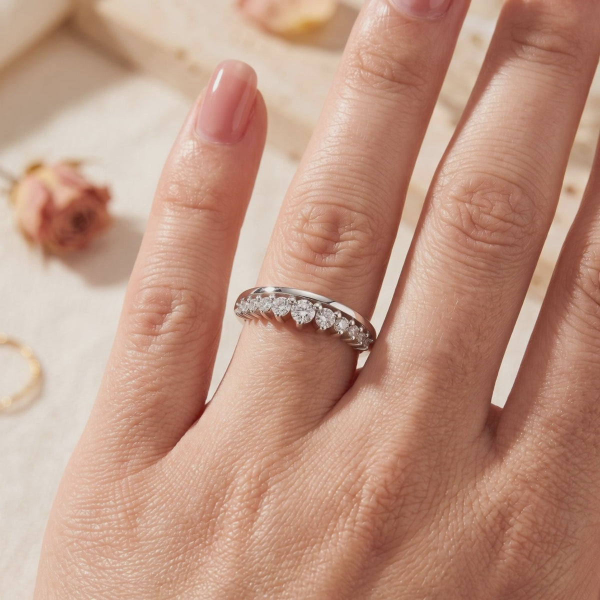 Silver curved ring with graduated clear round stones, worn on a hand.