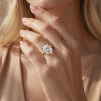 Cushion-cut solitaire ring with a gold-tone pavé band worn on a hand in soft lighting.