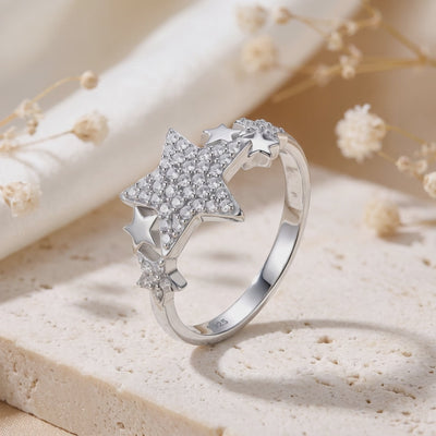 Angled silver star cluster ring displayed on a beige surface, with pavé stars and a visible S925 inner-band stamp.