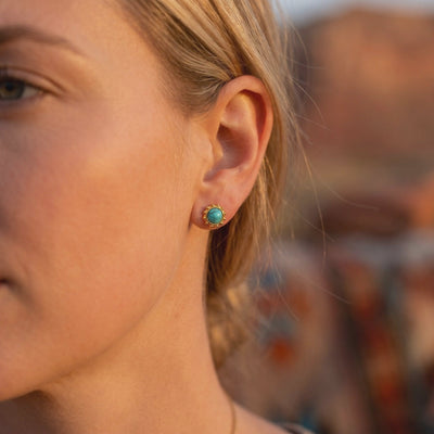 Close-up side view of a woman wearing a gold-tone turquoise-colored stud earring with a dotted bezel.
