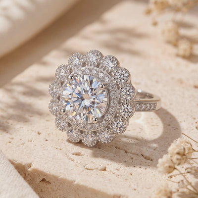 Close-up view of the silver flower halo ring featuring a round center stone on a beige stone slab.