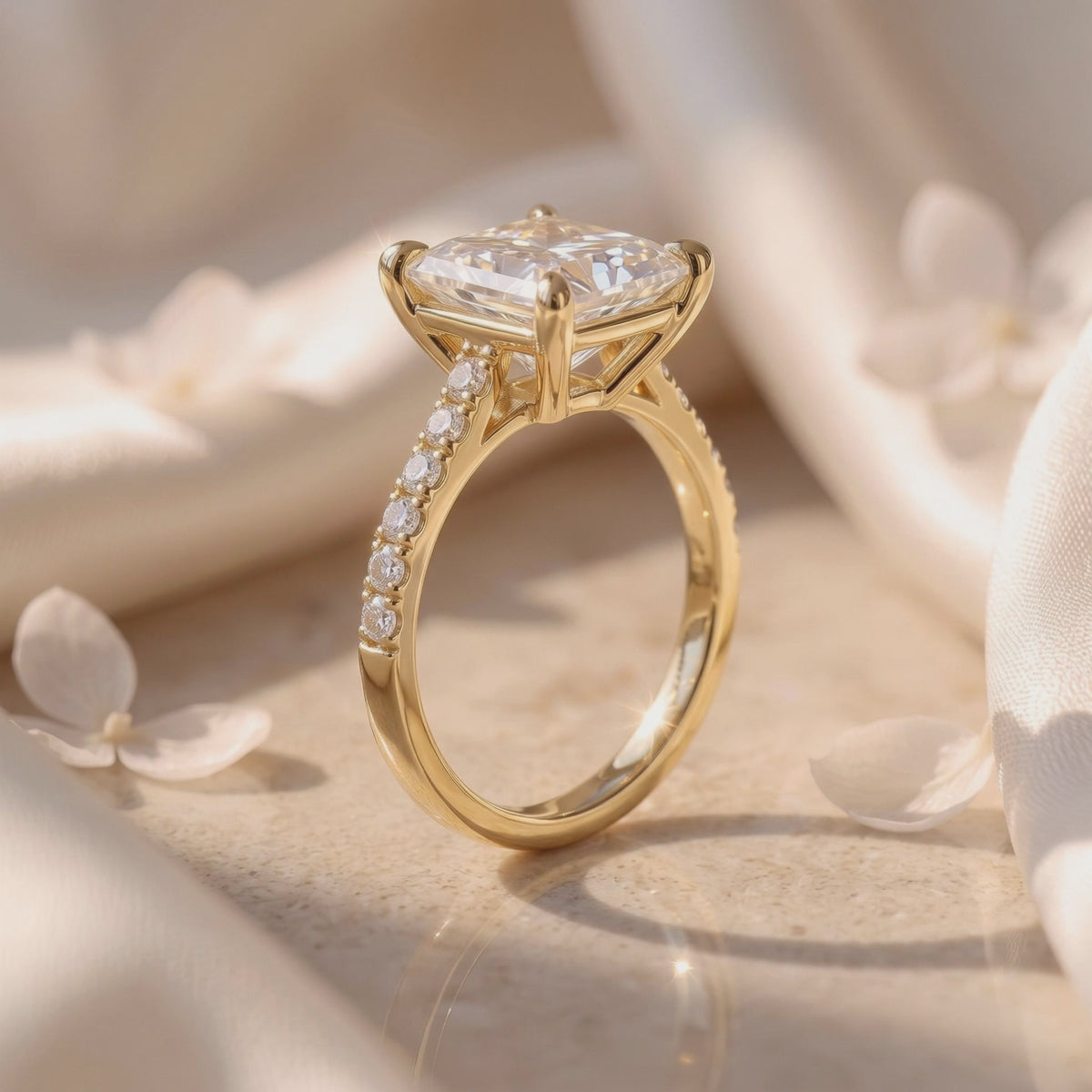 Side profile of a yellow gold-toned princess-cut solitaire ring resting on draped fabric among flower petals.