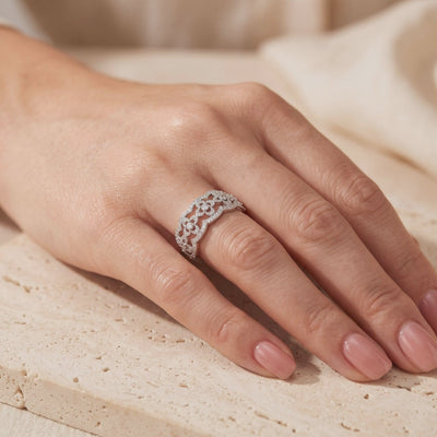 Hand wearing a silver clover lattice ring on a textured beige stone surface