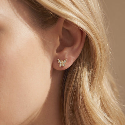 Gold-toned butterfly stud earring with round stones worn on an earlobe, shown in close-up.