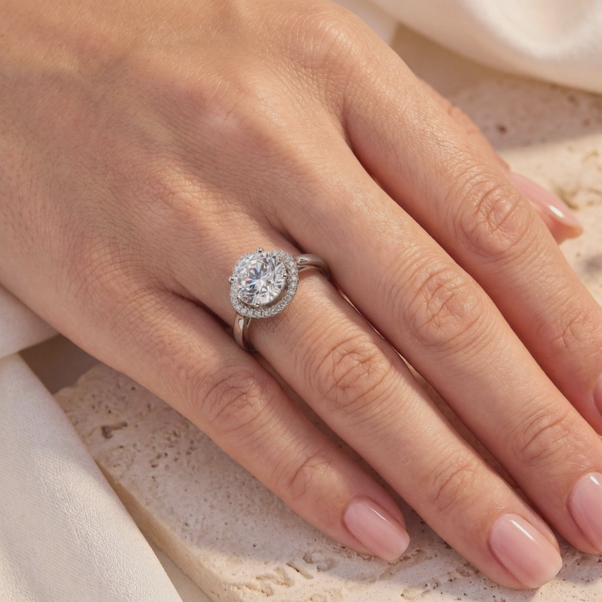 Hand wearing a silver halo ring with a round clear center stone and pavé accents.