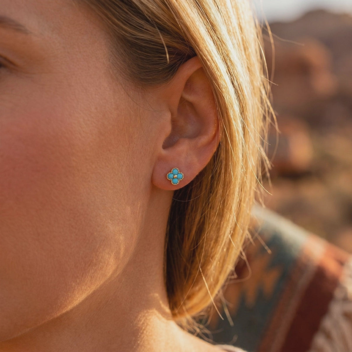 Close-up of a model wearing a gold-toned four-petal turquoise stud earring.