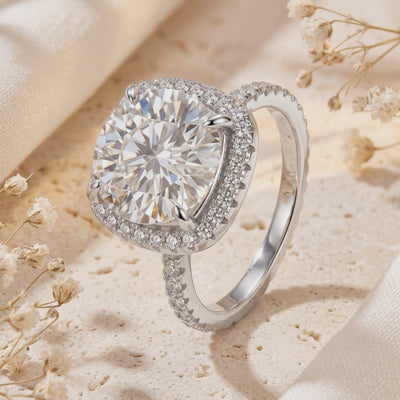 Angled view of a silver ring with a round center stone surrounded by a cushion pave halo and pave band.