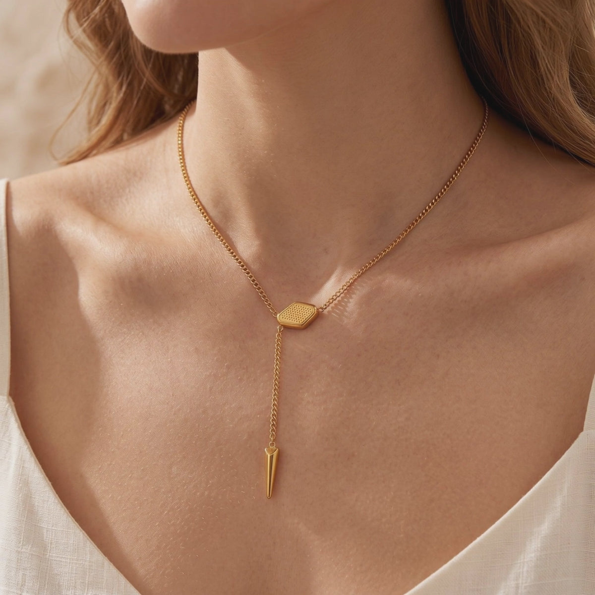 Gold-tone lariat necklace with a textured hexagonal slider and spike pendant, worn on a model.