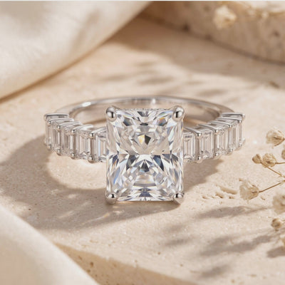 Close-up of the silver Ismerie ring resting on a pale textured surface, showing its radiant-cut center and side accents.