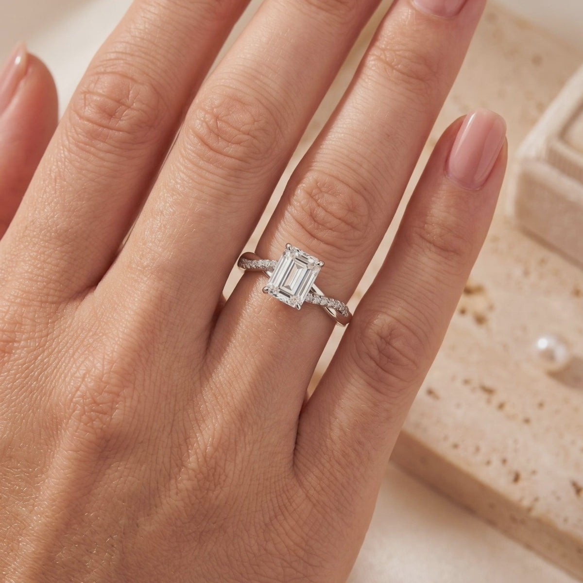 Emerald-cut silver solitaire ring with a twisted pavé band worn on a hand.