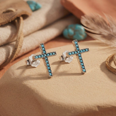 Pair of silver cross earrings with blue stones and S925-stamped backs on a tan surface