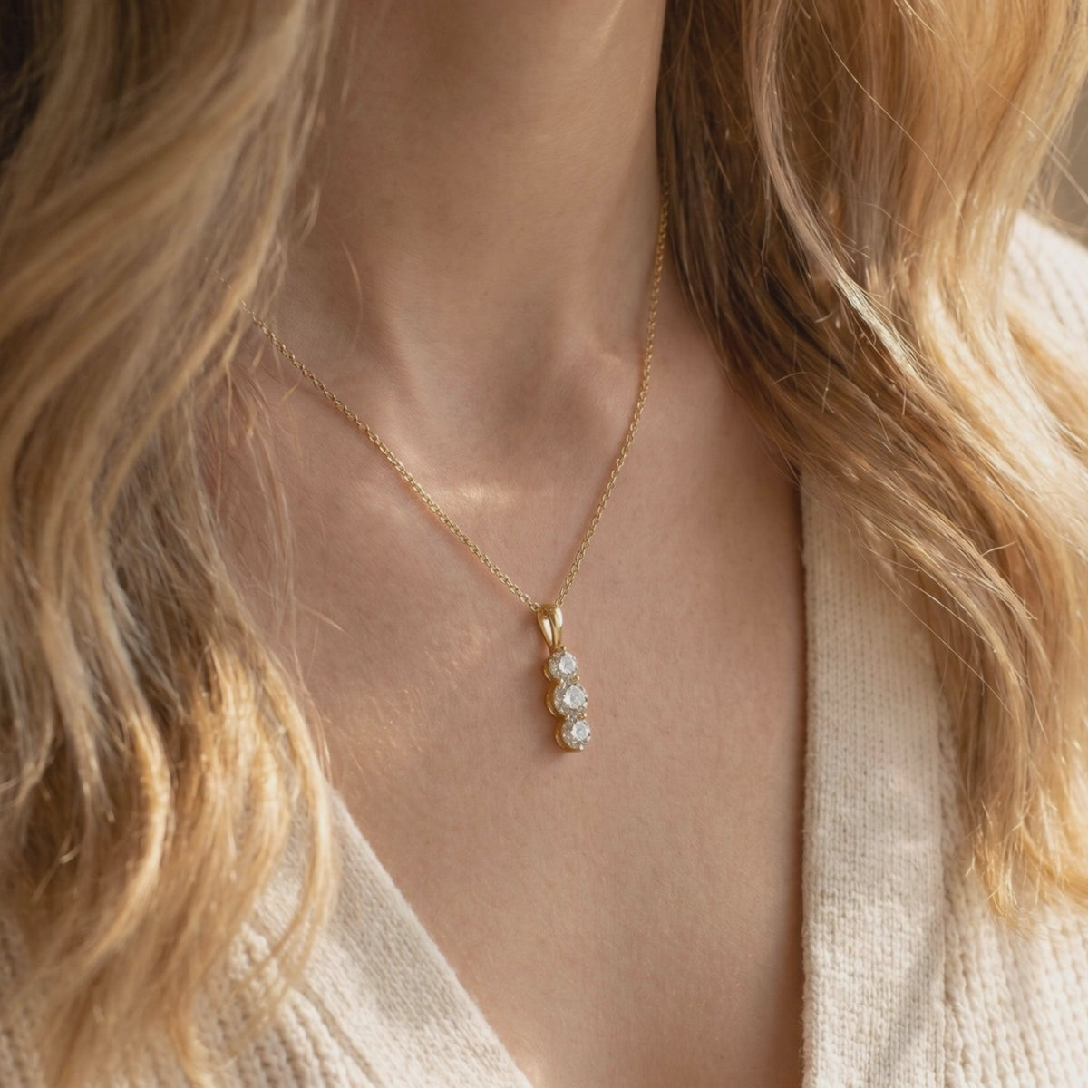 Gold-tone necklace with a vertical three-stone drop pendant worn on a model's collarbone.