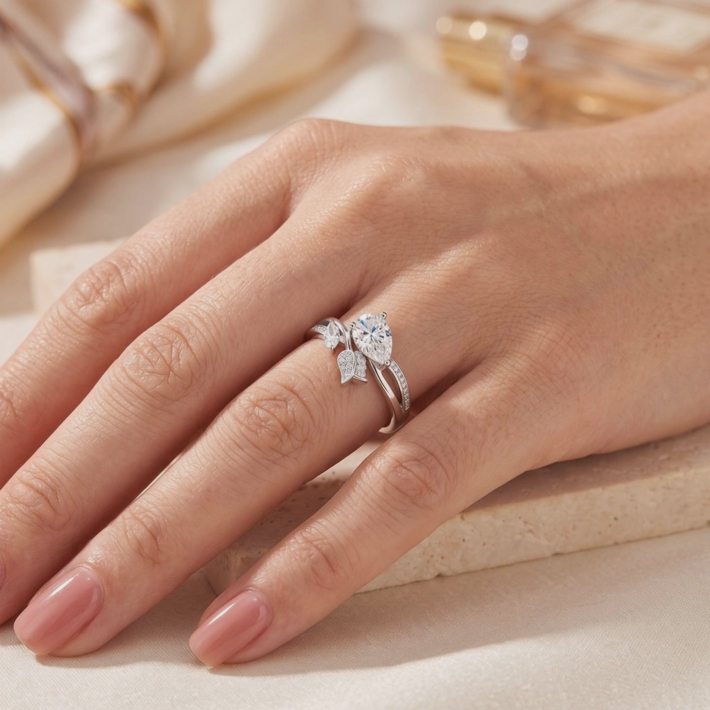 Silver leaf bypass ring with a pear-shaped clear center stone shown worn on a finger.