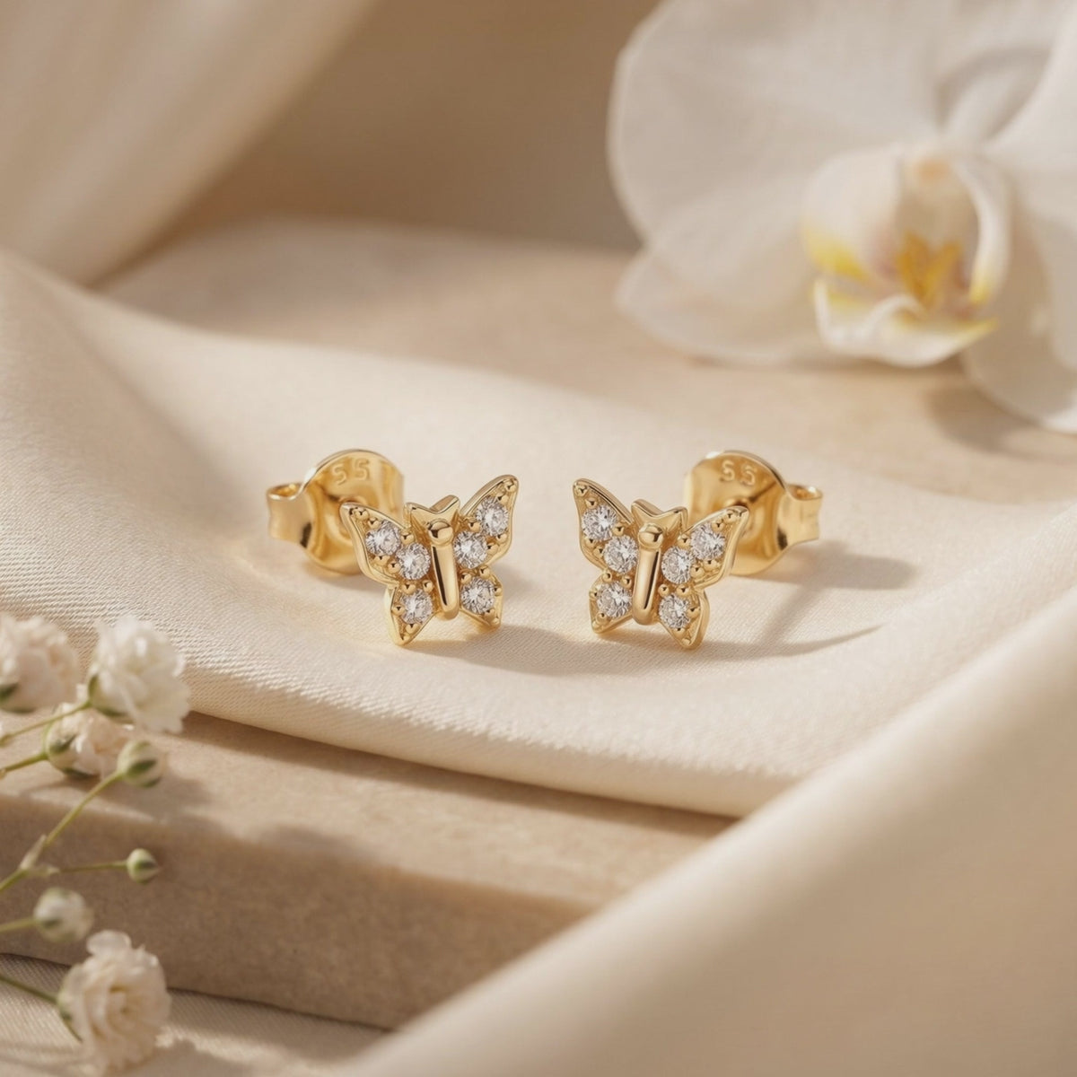 Pair of gold-toned butterfly stud earrings with round stones displayed on cream-colored fabric.