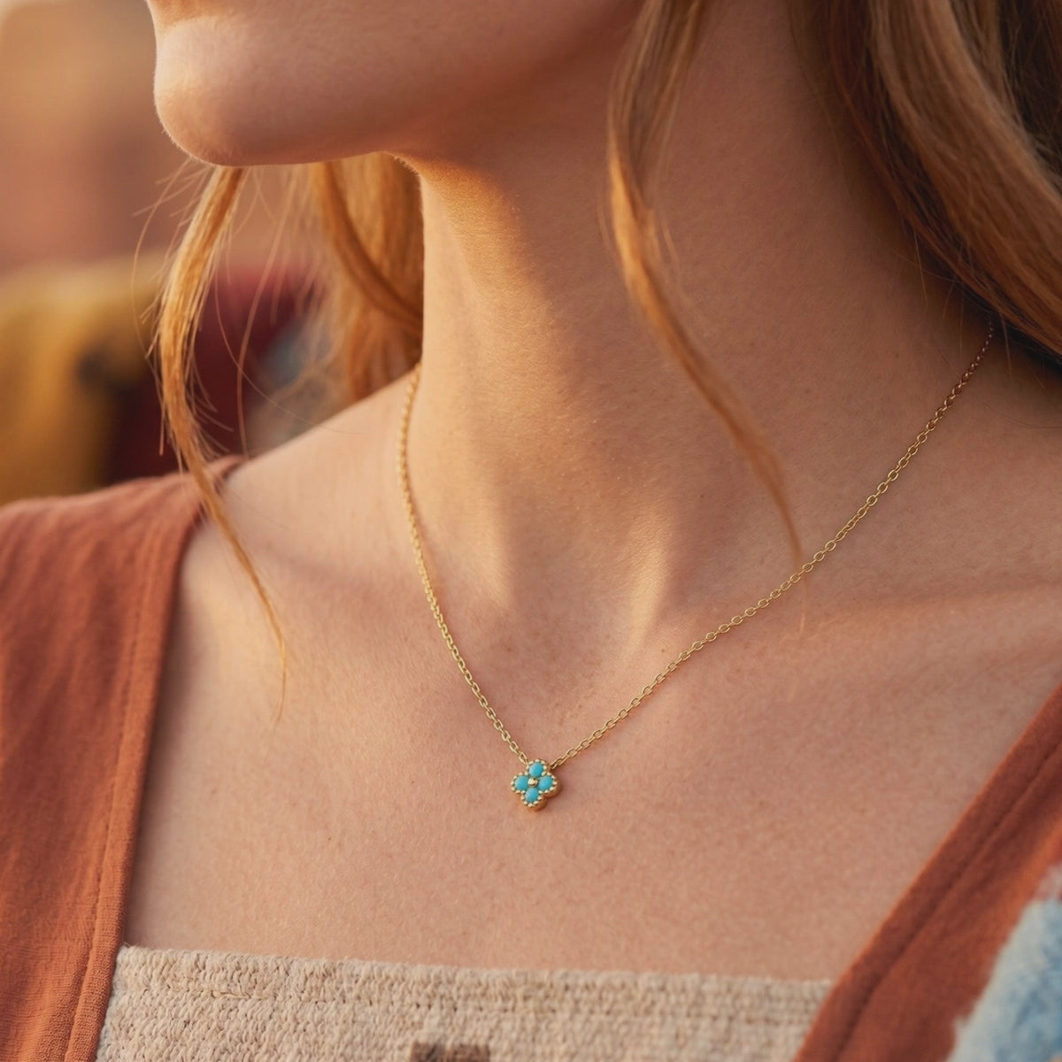Woman wearing a gold chain necklace with a small flower-shaped pendant set with four turquoise stones.