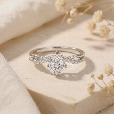 Sterling silver crown ring with a round moissanite displayed front-on on a beige stone surface with dried flowers.