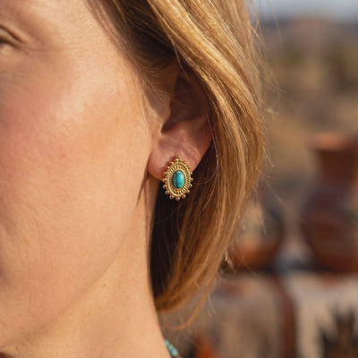 Side view of a model wearing a gold-tone oval earring with a turquoise cabochon and textured beaded border.