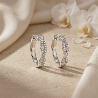 Pair of twisted silver hoop earrings with pavé moissanite accents displayed upright on a stone surface