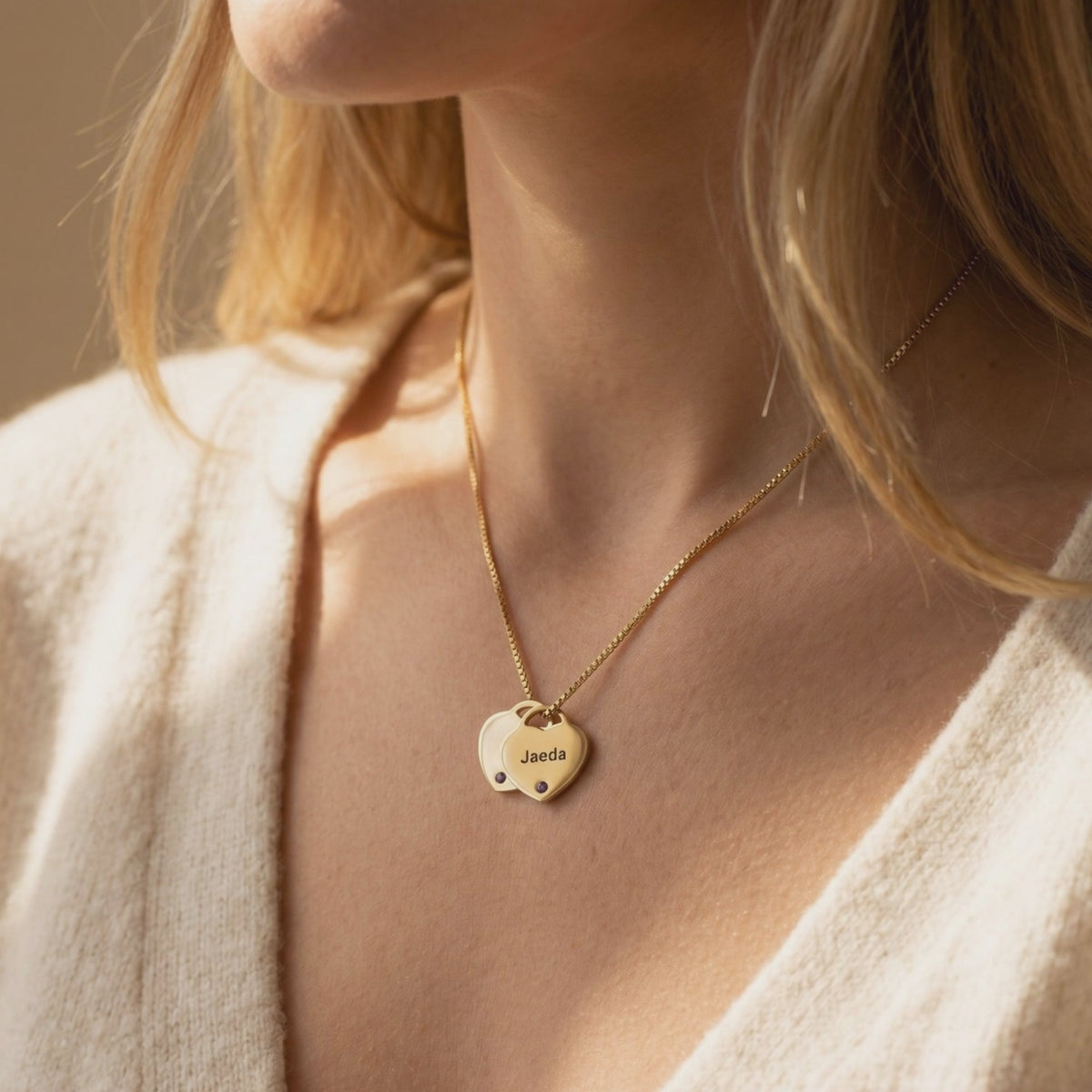 Gold-tone necklace worn on a woman’s neck with two overlapping heart pendants; the front pendant is engraved “Jaeda”.