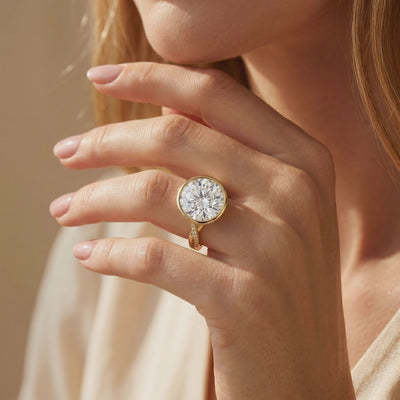 Yellow gold-toned bezel ring worn on a hand, with a large round center stone and twisted pavé band.
