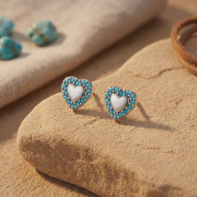 Pair of heart-shaped turquoise earrings with light centers resting on a tan stone surface.
