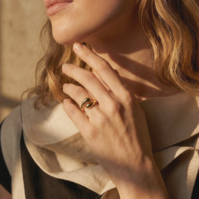 Gold-tone open bypass ring with rounded ends, worn on a hand beside a person's chin.