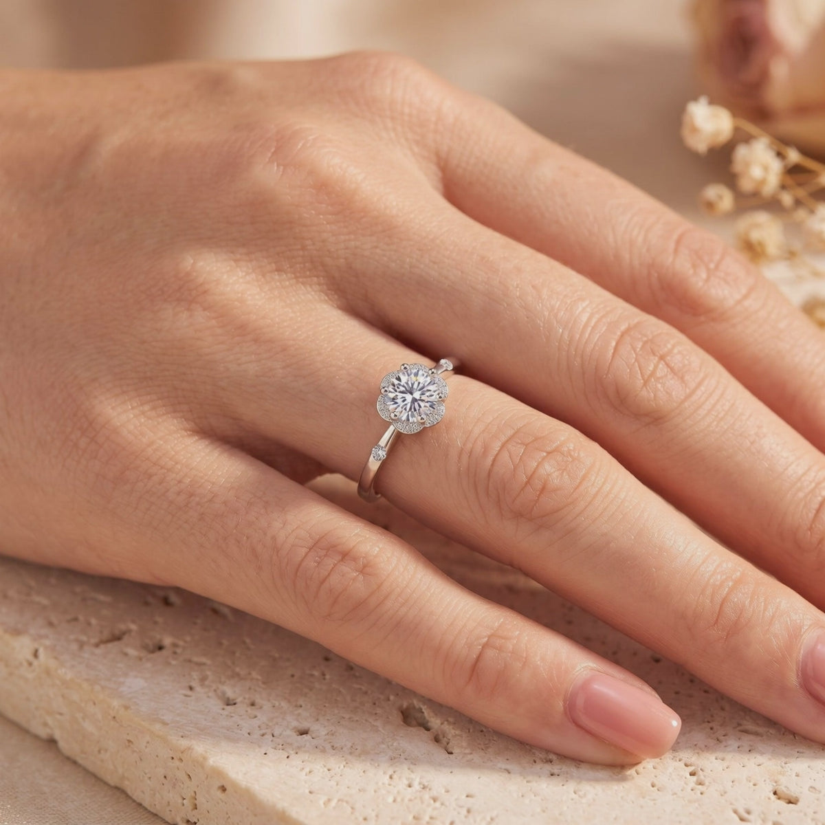 Silver flower halo ring with a round clear center stone, shown worn on a hand.
