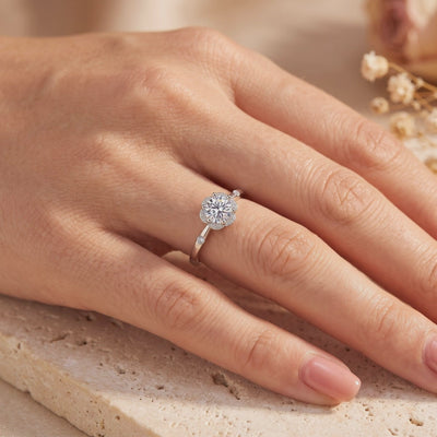 Silver flower halo ring with a round clear center stone, shown worn on a hand.