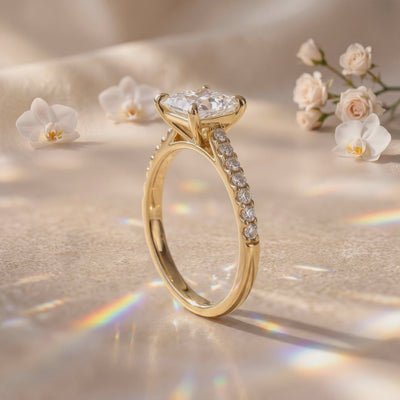 Gold-tone pavé solitaire ring standing upright on a reflective surface, showing the elevated princess-cut stone in side view.