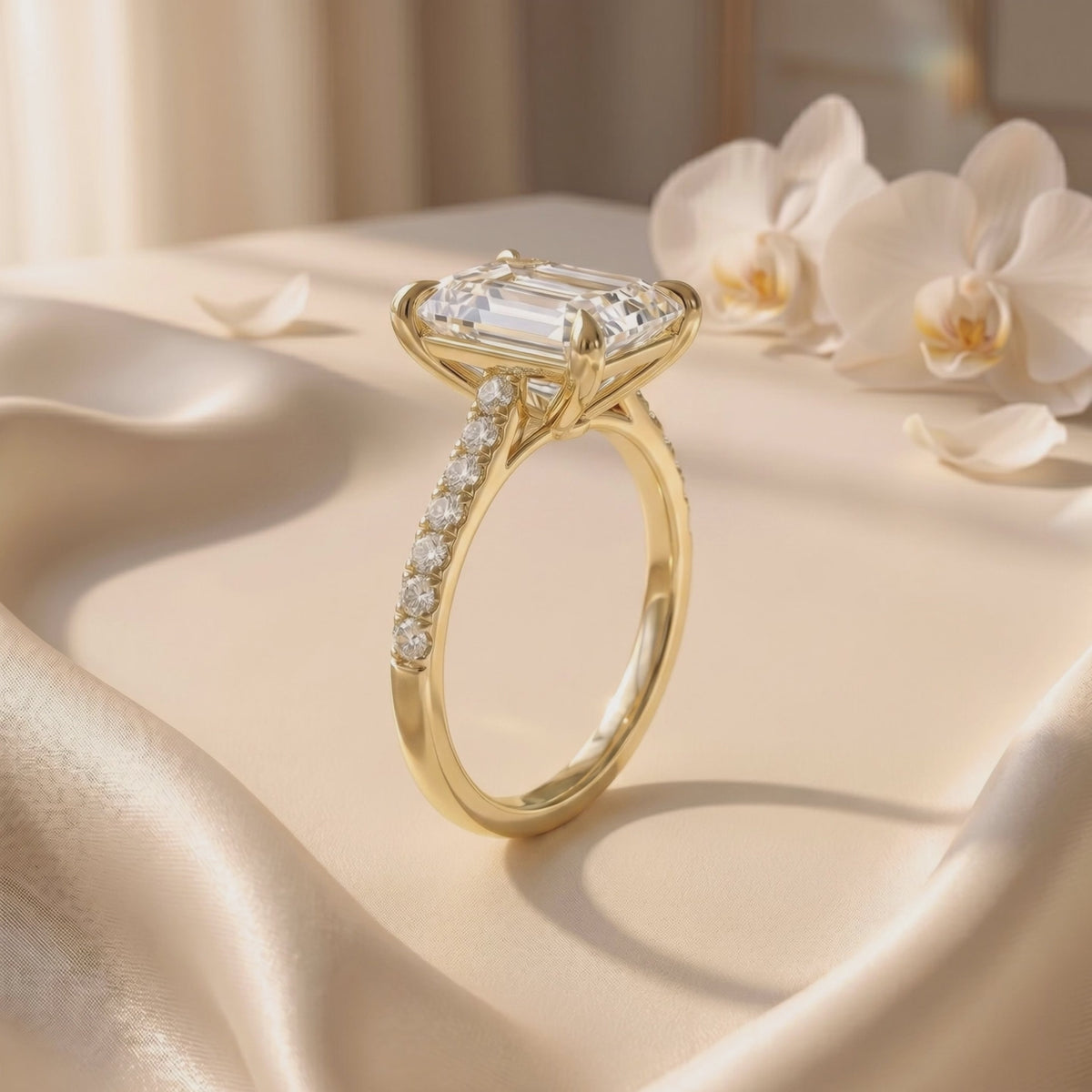 Yellow-toned emerald-cut pavé solitaire ring shown in side view on satin fabric, with orchids in the background.