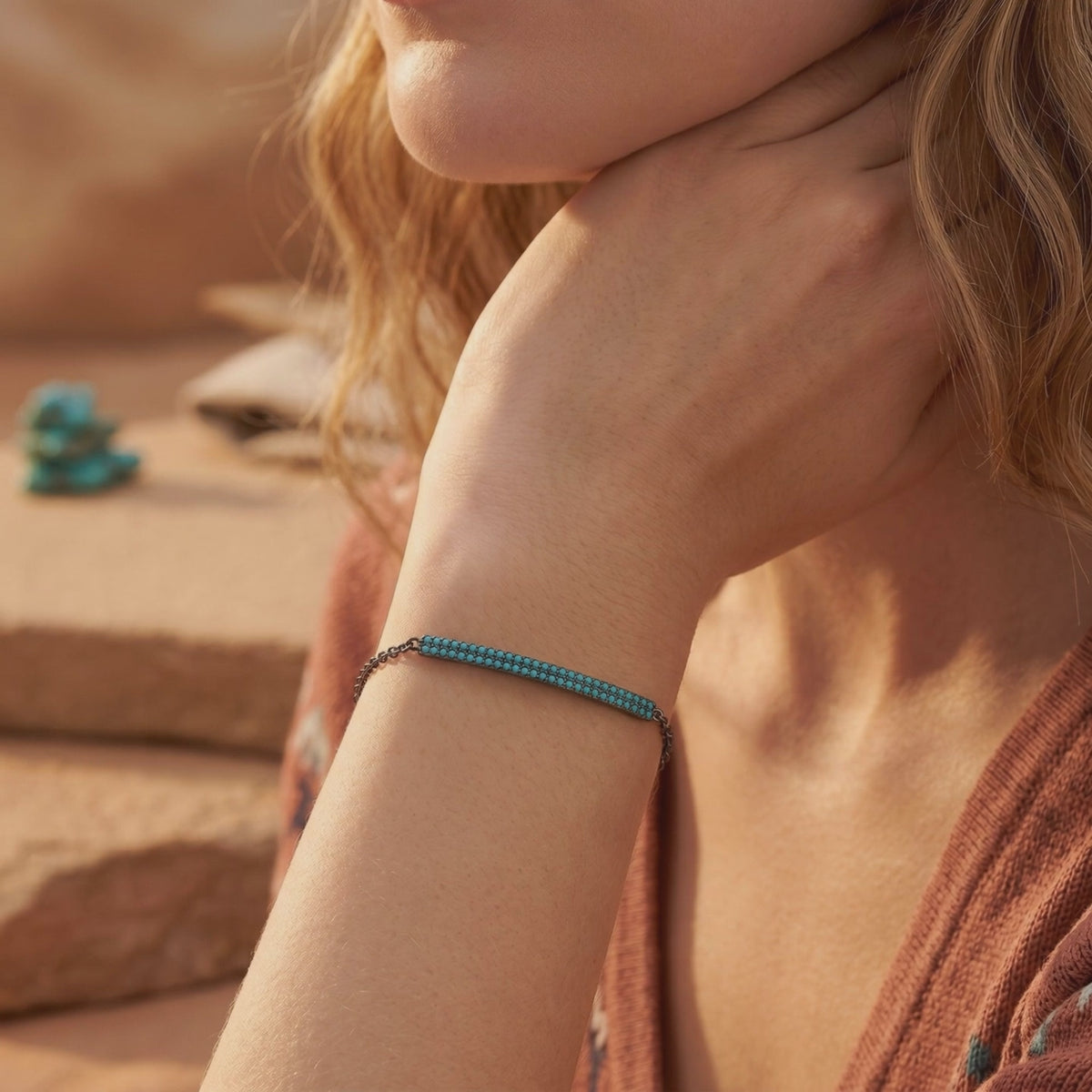 Woman wearing a dark silver chain bracelet with a double-row turquoise bar against warm desert-toned rocks.