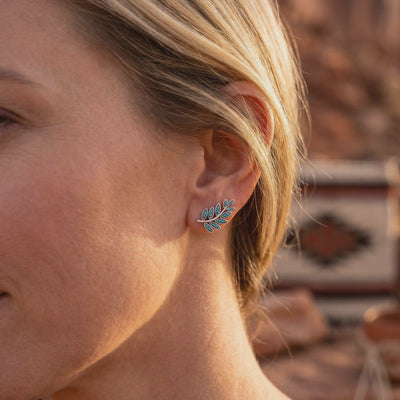 A silver leaf-branch earring with multiple turquoise stones worn on a woman's ear.