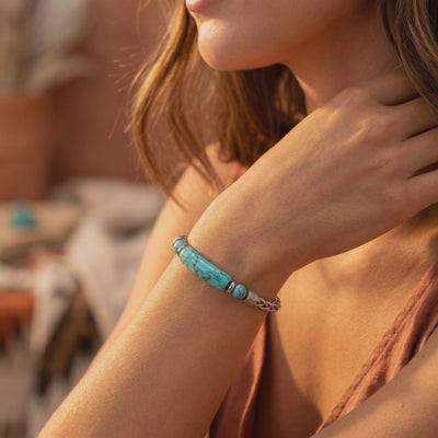 Woman wearing the bracelet, showing its turquoise-hued matrix bar, round beads, and chain links.