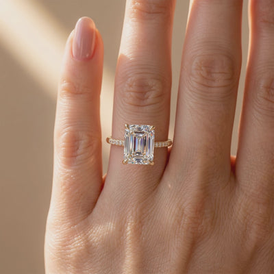 Top view of a yellow-gold-tone ring worn on a hand, with a large emerald-cut moissanite and pavé band.