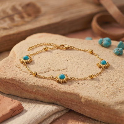 Gold-tone station bracelet with sunburst turquoise-colored stones displayed on a textured stone slab.