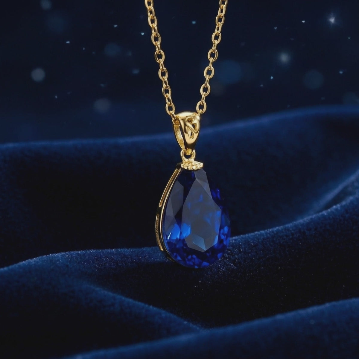 Close-up of a faceted pear-shaped simulated sapphire pendant necklace in solid gold on dark blue velvet.