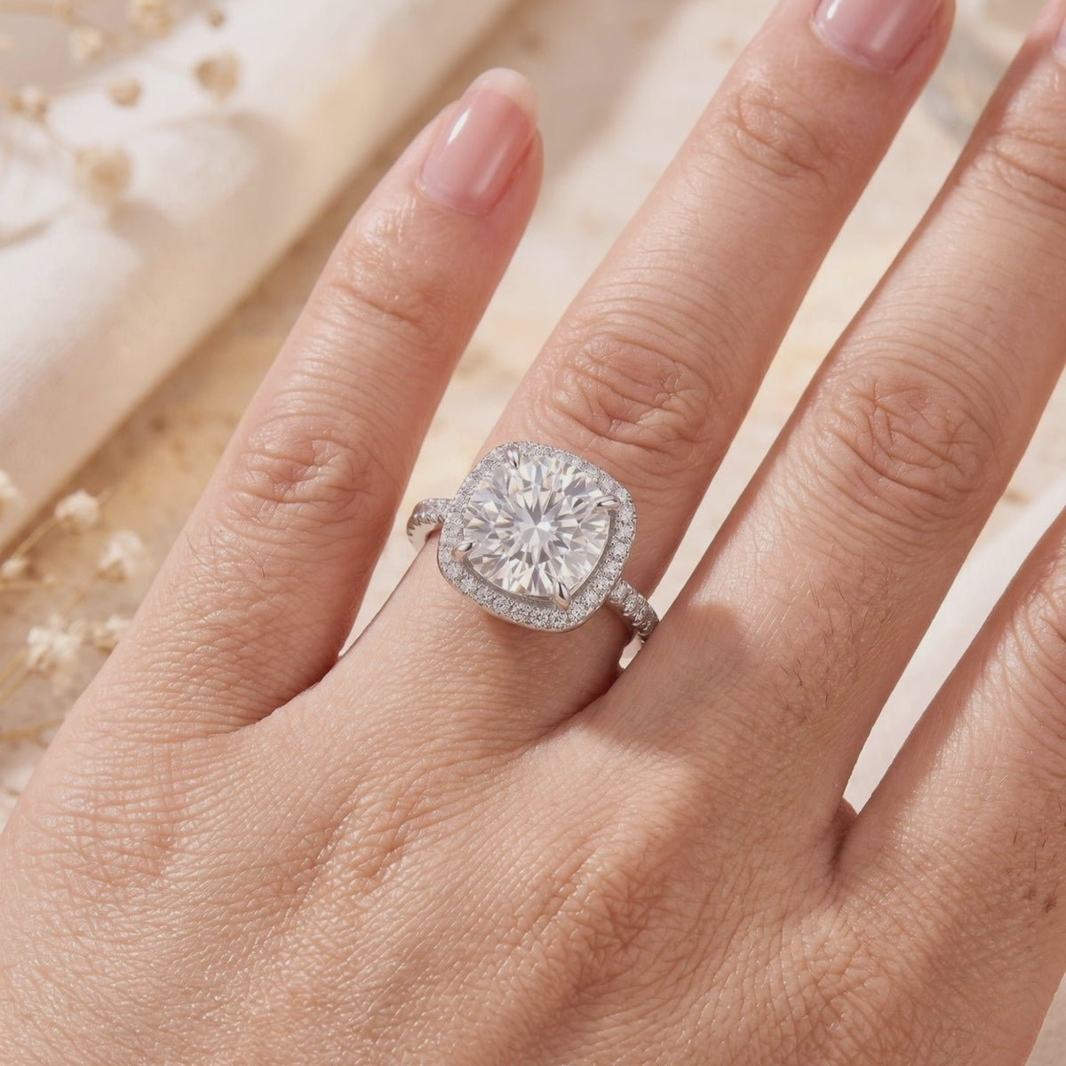 Top view of a hand wearing a silver ring with a large round stone set in a cushion pave halo.