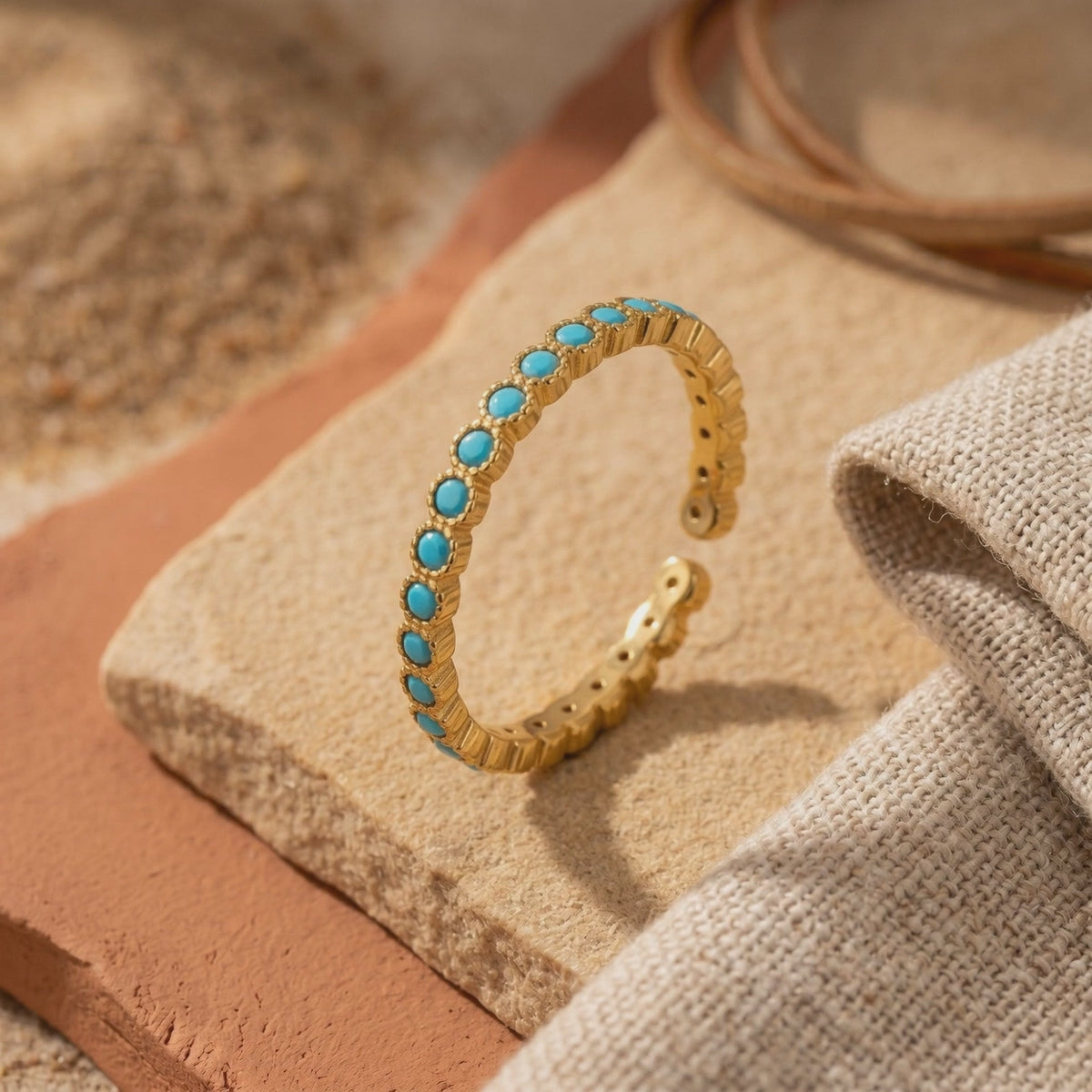 Gold-tone open-back ring with round turquoise cabochons displayed on a light tan stone slab.