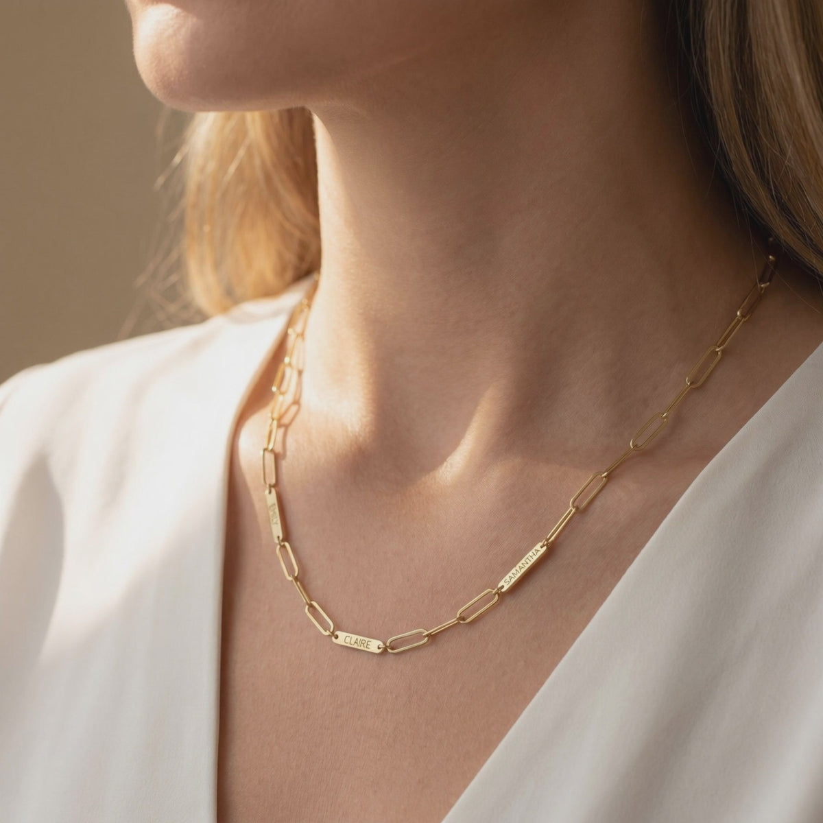 Gold link chain necklace with engraved name tags worn around a model’s neck.