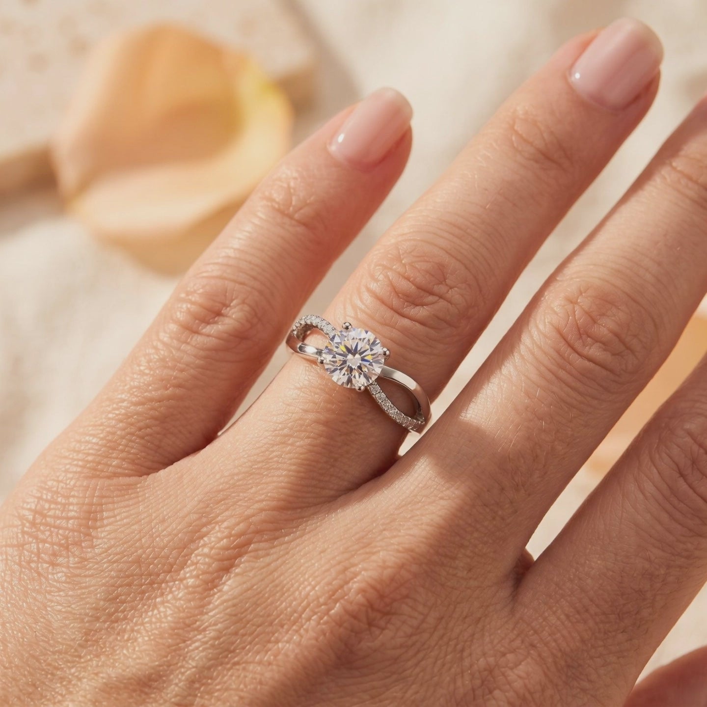Silver crisscross ring with a round center stone and pavé accents worn on a finger.