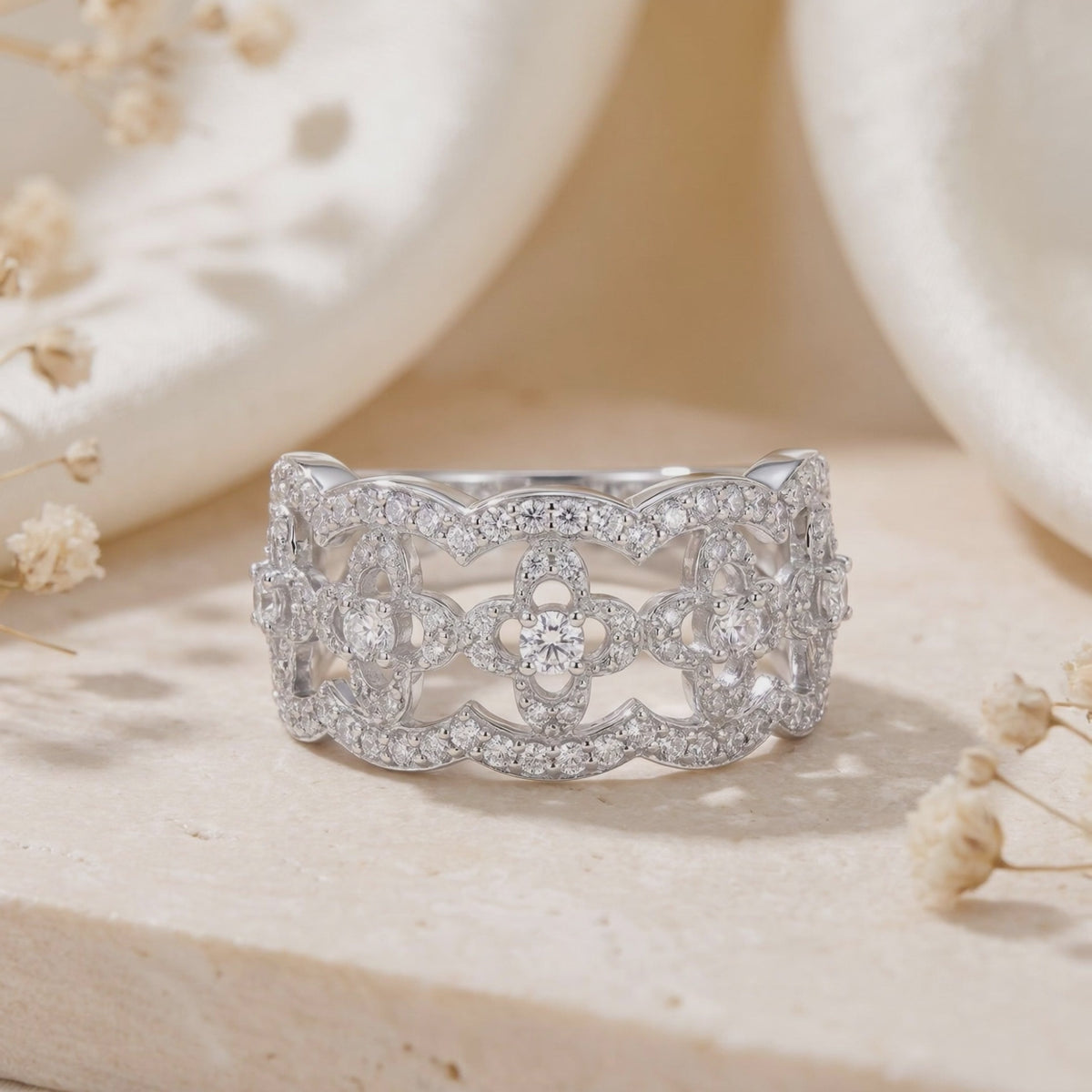 Close-up of a silver open-work clover lattice ring with clear stones on a beige stone surface