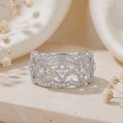 Close-up of a silver open-work clover lattice ring with clear stones on a beige stone surface