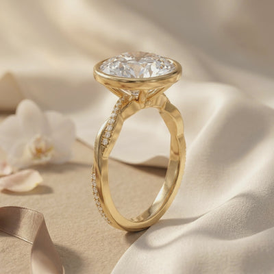 Side profile of a yellow gold-toned bezel ring with a raised round stone and twisted pavé band on draped fabric.