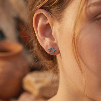 Silver open star stud earring with turquoise pavé stones, shown worn on a model's earlobe.
